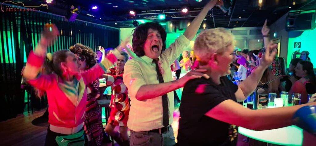 FEEST Bingo 1 1100x508 - Kamer van Feesthandel Deelnemers lopen vrolijk in een polonaise tijdens een uitbundige feestbingo vol meezingers, gezelligheid en een energieke feestsfeer